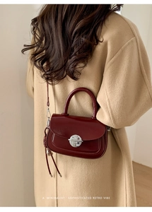 Retro burgundy shoulder bag with silver buckle worn by a model in a camel coat