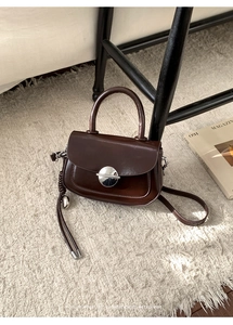 Detail of a dark brown mini handbag with silver round buckle on beige carpet