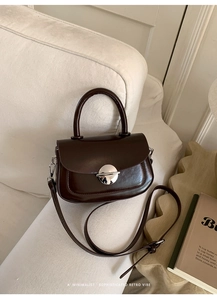 Detail of a dark brown retro crossbody bag featuring a glossy leather finish and silver clasp