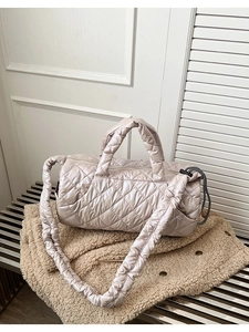 Detail of beige quilted puffer tote bag with thick padded strap on textured coat