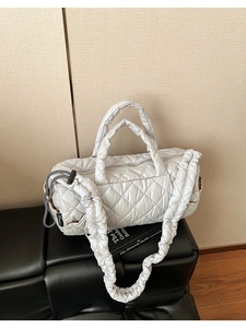 Detailed close-up of quilted light grey down tote bag with side pocket on black bench