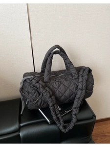 Detail of black quilted puffer barrel bag with gathered shoulder strap on leather bench