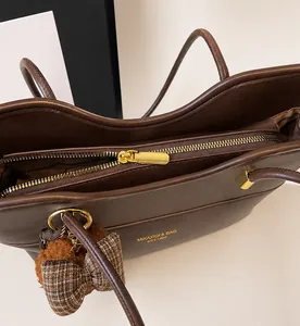 Close-up of vintage brown leather tote bag with gold zipper and bear pendant detail