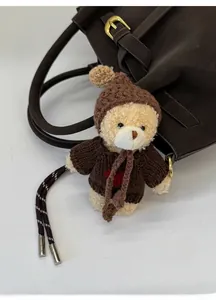 Detailed view of a beige teddy bear bag charm wearing a brown sweater with a red heart