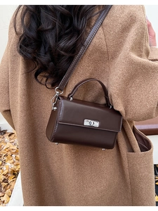 Detail van donkerbruine leren crossbodytas met zilveren sluiting op wollen jas