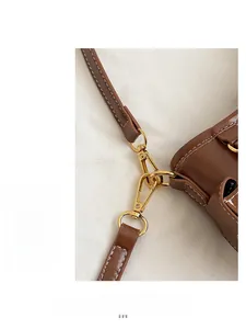 Dettaglio di borsa in pelle marrone con fibbia dorata e cuciture bianche a contrasto