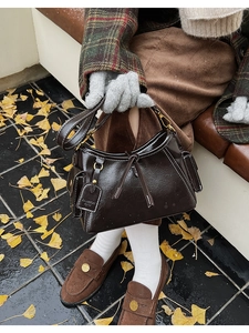 Dettaglio della borsa a secchiello vintage in pelle lucida marrone scuro con ciondolo