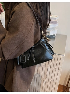 Dettaglio di una borsa a spalla in pelle nera con cuciture bianche e un ciondolo a fiocco