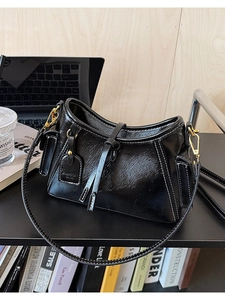 Dettaglio borsa in pelle lucida nera con cuciture bianche a contrasto e hardware dorato