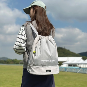 Dettaglio dello zaino in nylon grigio chiaro con logo Traveling light e ciondolo tennis
