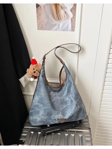 Macro detail of dark blue hobo bag texture with cute teddy bear charm on silver luggage