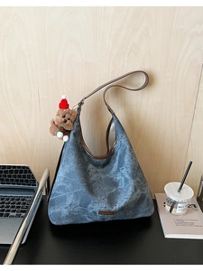 Detail of blue washed texture shoulder bag with brand plaque and cute teddy bear pendant