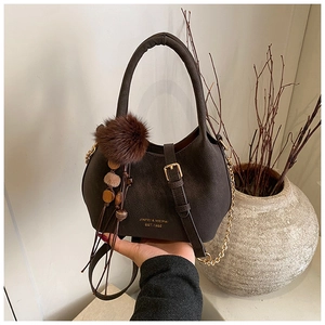 Détail du sac seau marron foncé avec pompon en peluche et bandoulière en chaîne dorée
