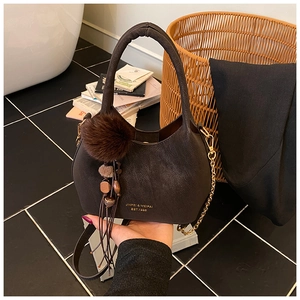 Détail d'un sac seau en cuir marron avec chaîne dorée et breloque en peluche douce