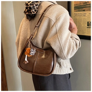 Braune Vintage-Schultertasche mit Leoparden-Plüsch-Anhänger, getragen von einem Model