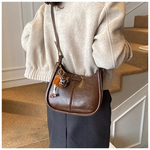 Detailansicht einer braunen Hobo-Tasche mit dekorativem Leoparden-Herz und Bommel-Anhänger