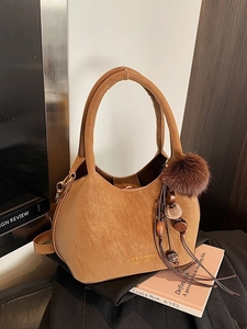Sac seau en cuir marron caramel avec poignée et pompon décoratif sur un bureau vintage