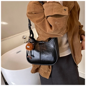 Detail der schwarzen Beuteltasche aus Leder mit braunem Plüsch-Monster-Anhänger