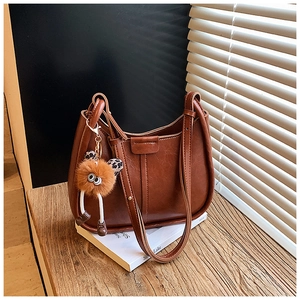 Braune Vintage-Eimertasche aus Leder mit Plüschanhänger auf einer Holzbank