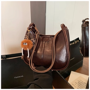 Detailansicht der glänzenden Leder-Eimertasche mit süßem Plüsch-Monsteranhänger und Schleife