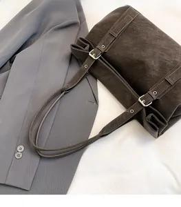 Detail of dark brown matte leather tote bag with silver buckles on grey suit background
