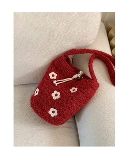 Gros plan sur un sac seau en tricot rouge avec des motifs floraux blancs en peluche
