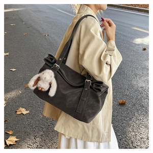 Detail of grey matte shoulder tote bag with cute plush rabbit charm in an outdoor setting