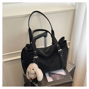 Detail of a large black matte tote bag with silver buckle straps and a rabbit plush charm