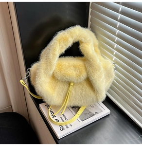 Detail einer gelben Plüschhandtasche mit Lederriemen auf weißen Büchern platziert