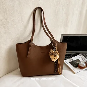 Detailed view of brown grain leather tote bag featuring a cute bear charm and logo