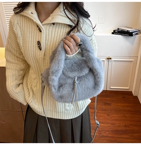 Detail der hellgrauen Webpelz-Handtasche mit Lederriemen auf cremefarbenem Pullover