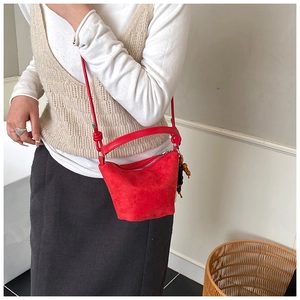 Detalle de bolso tipo cubo de ante rojo con cierre de cremallera y adorno de madera