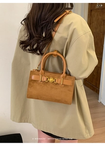 Detalle de un bolso bandolera retro marrón con hebilla de corazón dorado y textura de ante