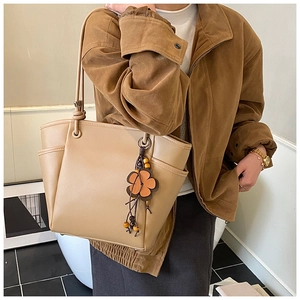 Dettaglio della borsa tote beige con tasca laterale e ciondolo a fiore in pelle elegante