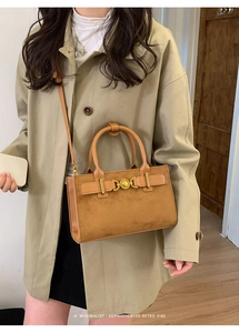 Bolso bandolera retro marrón con hebilla de corazón dorada sobre gabardina caqui