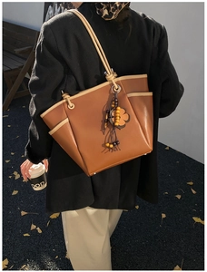 Dettaglio borsa tote in pelle marrone con bordi a contrasto e ciondolo a quadrifoglio