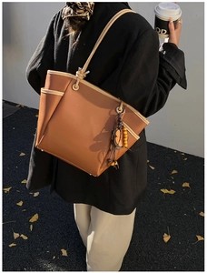 Dettaglio della borsa tote in pelle caramello con bordi beige e ciondolo di perline in legno
