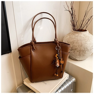 Dettaglio della borsa tote in pelle marrone scuro con manici annodati e ciondolo floreale