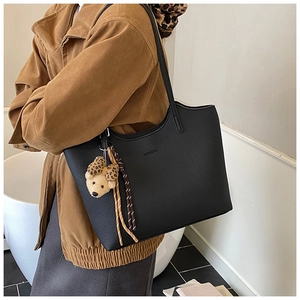 Detail of black pebbled leather tote bag featuring a cute bear charm and woven accents