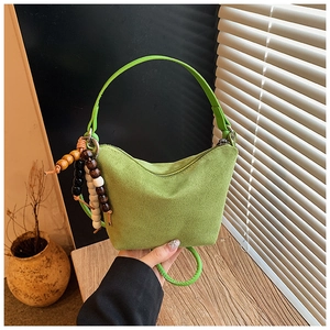 Detalle de bolso tipo cubo de ante verde con asa ancha y colgantes decorativos de madera