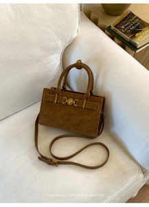 Detalle de bolso vintage marrón con cierre de corazón dorado sobre sofá blanco