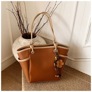 Dettaglio borsa shopper marrone con bordi a contrasto e ciondolo floreale su tappeto tessuto
