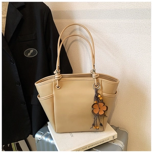 Dettaglio di una borsa tote beige con ciondolo a fiore su una valigia da viaggio