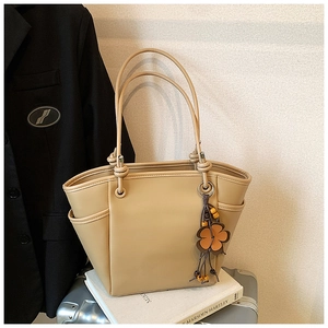Dettaglio borsa tote color albicocca in ecopelle con ciondolo floreale su una valigia
