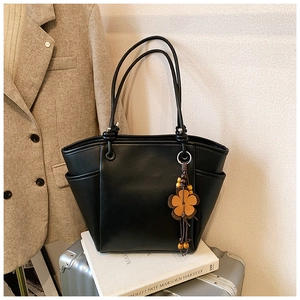 Dettaglio della borsa tote in pelle nera con ciondolo a fiore su uno sfondo stile di vita