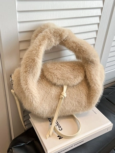 Elegante beige Plüsch-Handtasche mit Pelzgriff und Lederriemen auf einem weißen Buch