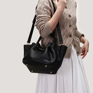 Detail of black pebbled leather tote bag showing gold protective studs and wide strap