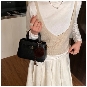 Detail of black woven texture shoulder bag with golden hardware and plush ball pendant