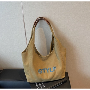 Detail view of mustard yellow canvas tote with blue embroidery and brown leather handles