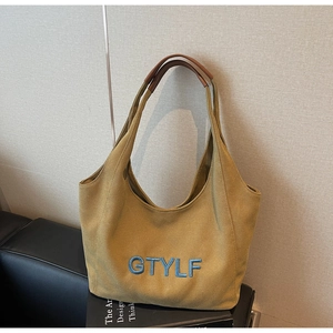 Close-up of khaki canvas tote bag with blue embroidered letters and leather handles